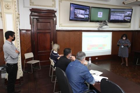 reunião com pessoas sentadas e em pé em sala com telões. #paratodosverem