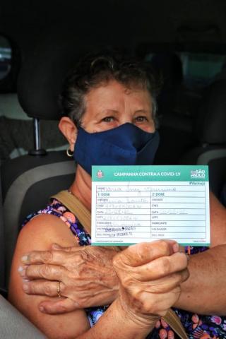 mulher sentada em banco de carro exibe comprovante de vacina. #paratodosverem