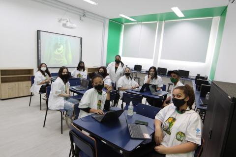 O grupo de alunos participantes do Jovem Doutor sentados em sala de aula, com um telão ao fundo. #paratodosverem