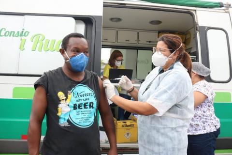 mulher vacina homem em frente à viatura do consultório na rua. #paratodosverem