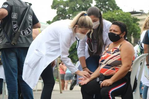 mulheres usando avental branco medem a pressão de uma mulher que está sentada. #paratodosverem