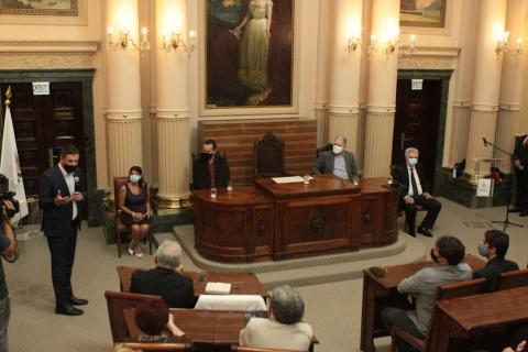 cerimônia na sala princesa isabel, com público sentado, o prefeito falando, em pé, e os homenageados sentados. #paratodosverem