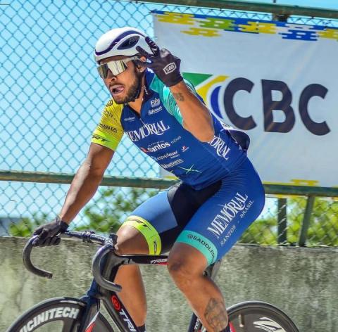 Atleta faz gesto com número 3 em cima da bicicleta #paratodosverem