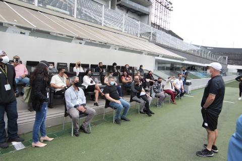 Homem fala com pessoas sentadas no banco de reserva do estádio #paratodosverem