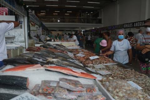 box com vários peixes expostos sobre gelo. Público está circulando do lado direito da foto. #paratodosverem