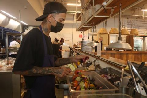 Cozinheiro prepara espetinho de legumes no restaurante paru. Ele usa avental e boné. #paratodosverem