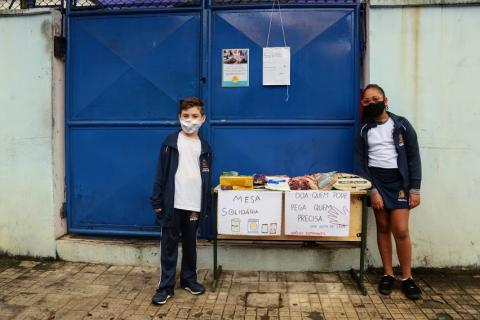 alunos estão em torno de mesa com alimentos. #paratodosverem