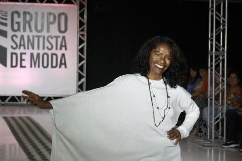 Mulher negra, com vestido branco, faz pose na passarela durante desfile. #pratodosverem