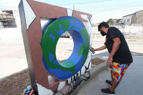 Homem grafita mureta com desenho do planeta Terra. #paratodosverem