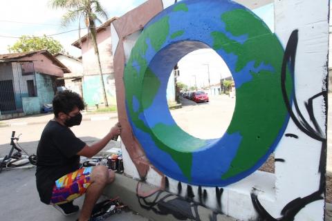 homem grafita mureta com arte do planeta Terra. #paratodosverem