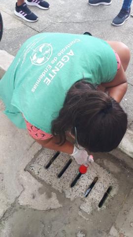 mulher aponta lanterna para bueiro no meio-fio. #paratodosverem