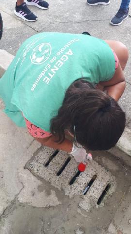 mulher aponta lanterna para bueiro no meio-fio. #paratodosverem