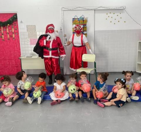 Papai e Mamãe Noel posam para foto atrás de crianças. #paratodosverem