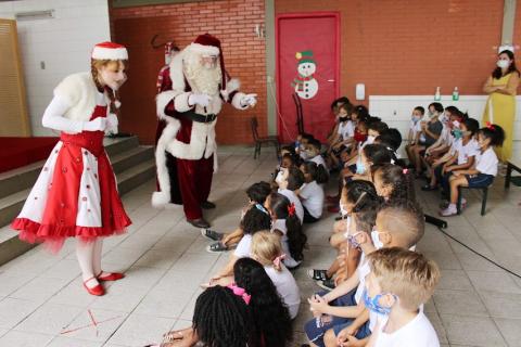 Papai e Mamãe Noel interagem com crianças. #paratodosverem