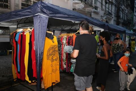 público para em frente a tenda onde estão penduradas peças de roupas. #paratodosverem