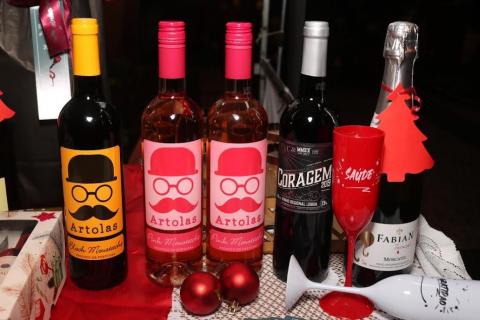 garrafas de vinho sobre uma mesa onde também estão duas taças e duas bolas de natal. #paratodosverem