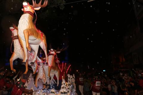 duas grande renas em carro alegórico puxam o trenó com o papai noel. O grande público está na rua. #paratodosverem