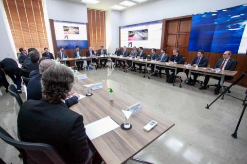 sala de reuniões com várias pessoas sentadas em mesa em formato de U. #paratodosverem