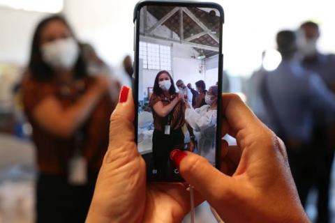 Mãos seguram smartphone para fotografar pessoa sendo vacinada. #paratodosverem