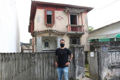 Homem posa para foto na frente de casa antiga #paratodosverem