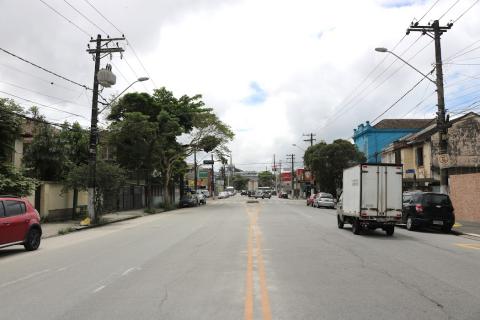 Foto de uma via com veiculos estacionados e caminhão passando #paratodosverem