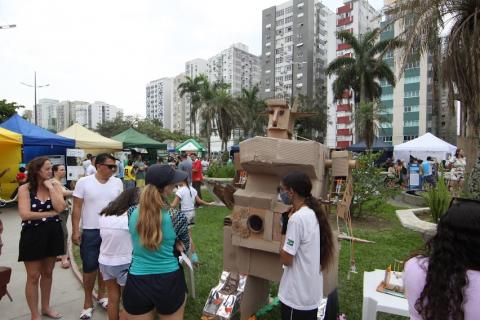 pessoas olham boneco feito de materiais recicláveis #paratodosverem 