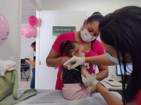Criança é segurada pela mãe enquanto toma vacina #paratodosverem