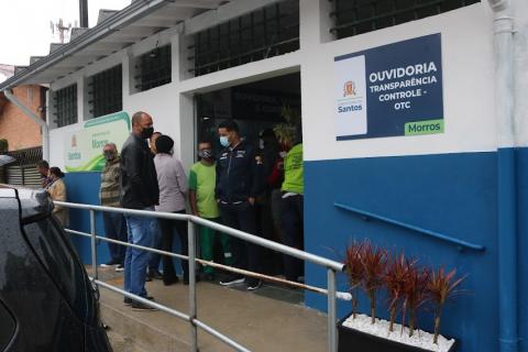 Frente da subprefeitura com placa da ouvidoria e várias pessoas. #paratodosverem