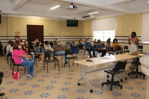 salão com várias pessoas sentadas assistindo a palestra dada por uma mulher que está em pé. #paratodosverem