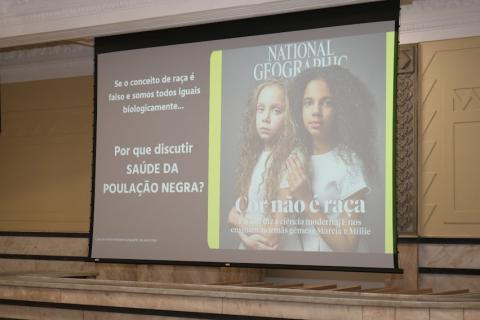 projeção em telão onde se vê capa de revista com a foto de duas meninas, branca e negra, e se lê Cor não é raça. #paratodosverem