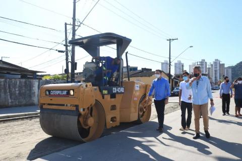 máquina compactadora está próxima ao meio-fio. Homens caminham na calçada. #paratodosverem