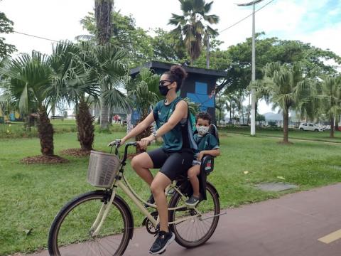 mulher pedala na ciclovia levando filho em cadeirinha acoplada na garupa. #paratodosverem