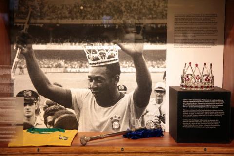 Foto de Pelé com coroa e cetro na mão. Ao lado, a coroa e o cetro originais. #paratodosverem
