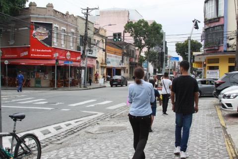duas pessoas andando em rua com varios comércios  #paratodosverem