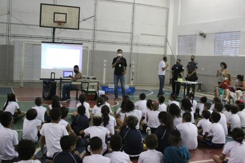 crianças estão sentadas na quadra da escola assistindo palestra. #paratodosverem