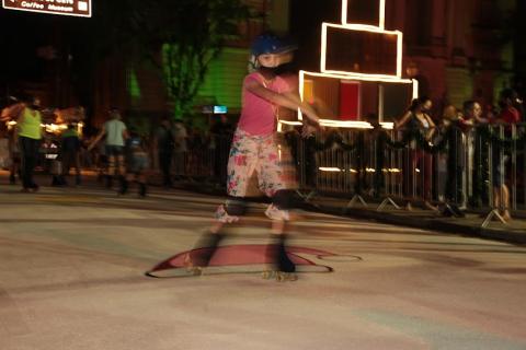 Menina se diverte em pista de patinação ao ar livre à noite. #paratodosverem