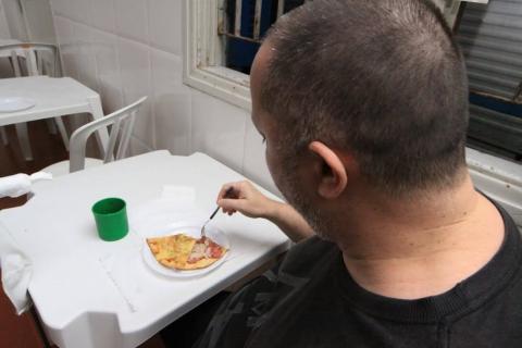 homem, de costas para foto, dá uma garfada em pedaço de pizza no prato. #paratodosverem