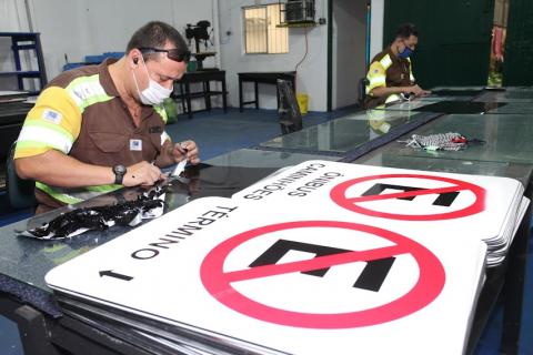 homem uniformizado trabalhando sobre chapas e diante de várias placas de proibição de estacionamento. #paratodosverem