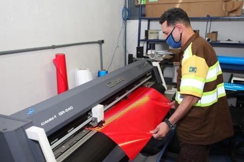 homem trabalham em máquina onde passa uma especie de plástico para ser usado nas placas. #paratodosverem