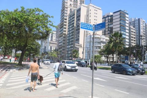 em primeiro plano, duas placas de identificação de alameda na praia num pequeno poste. Pessoas estão cruzando o trecho. #paratodosverem