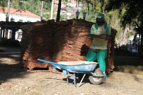 homem segura bloco de grama diante de um carrinho de mão. Atrás dele três pilhas de blocos de grama. #paratodosverem