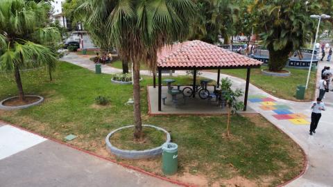 vista aérea da praça, com área ajardinada, gazebo ao centro, amarelinha pintada no chão e vegetação. #paratodosverem