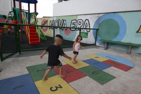 duas crianças pulam sobre amarelinha pintada no piso. #paratodosverem