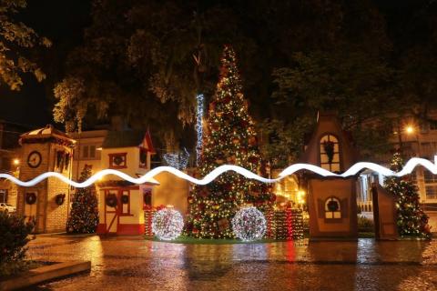 a decoração da praça com as casinhas ao fundo e uma árvore de natal. Há efeito de luz sobre a foto denominado light painting. #paratodosverem
