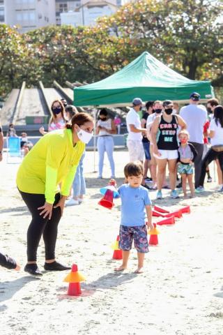 Criança se diverte ultrapassando cones na areia. #paratodosverem