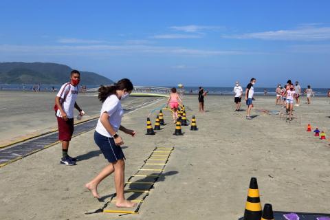 criança pula em estrutura de madeira estendida na areia. #paratodosverem