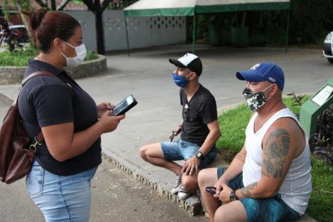 Agente da ouvidoria conversa com dois homens sentados no parque. #Paratodosverem