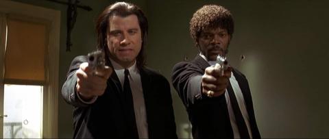 Dois homens apontam as respectivas armas de fogo posando de frente para a foto, em cena de pulp fiction. #paratodosverem