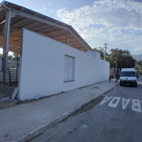 Fachada com muro branco e cobertura da quadra ao fundo. #pratodosverem