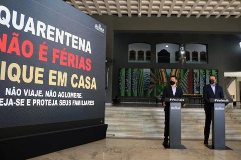 gRANDE TELÃO à esquerda onde se lê: quarentena não é férias fique em casa não viaje não aglomere proteja-se e proteja seus familiares. #Paratodosverem